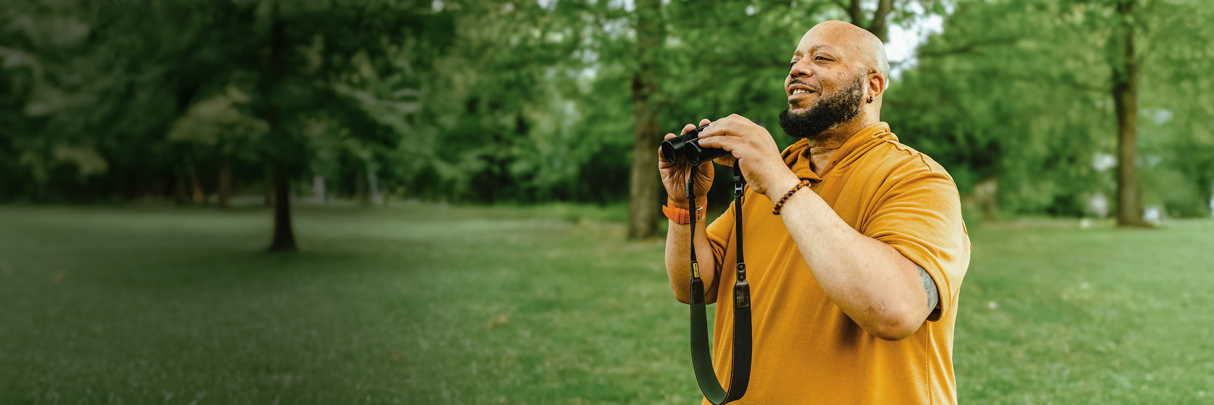 Al, a PYLARIFY patient, standing outside in nature, holding binoculars