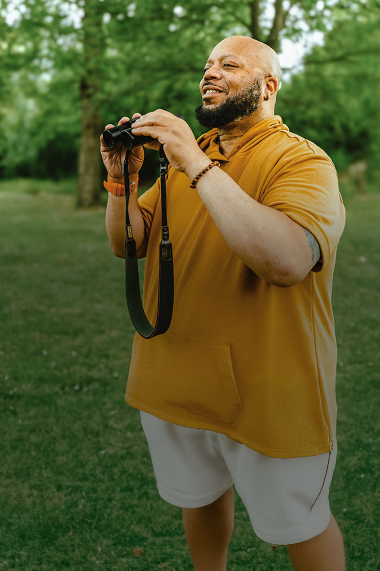 Al, a PYLARIFY patient, standing outside in nature, holding binoculars