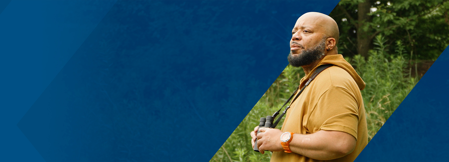 Al, a PYLARIFY patient, standing outside in nature, holding binoculars